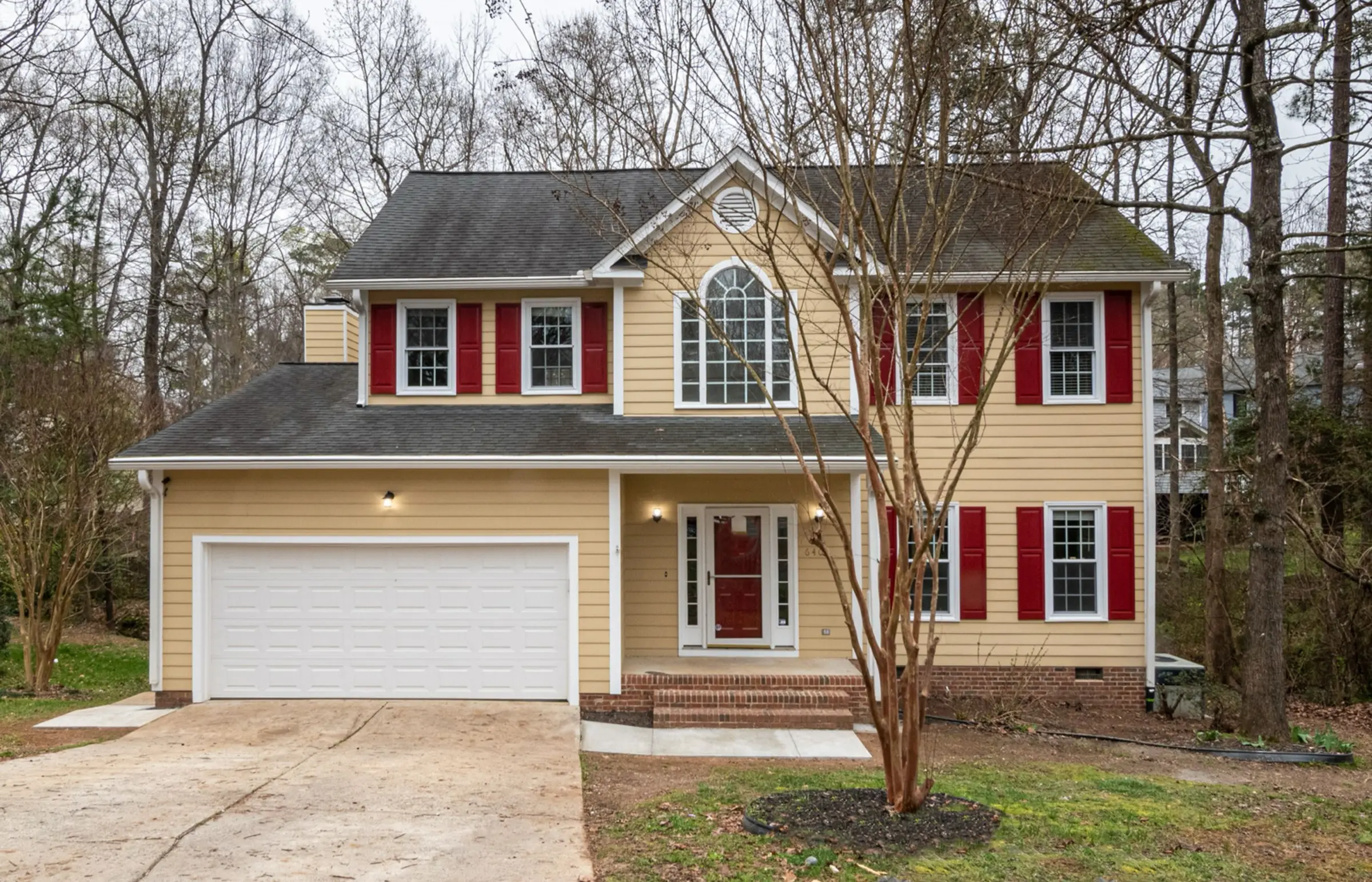 Yellow two-story colonial with red shutters and a two-car garage