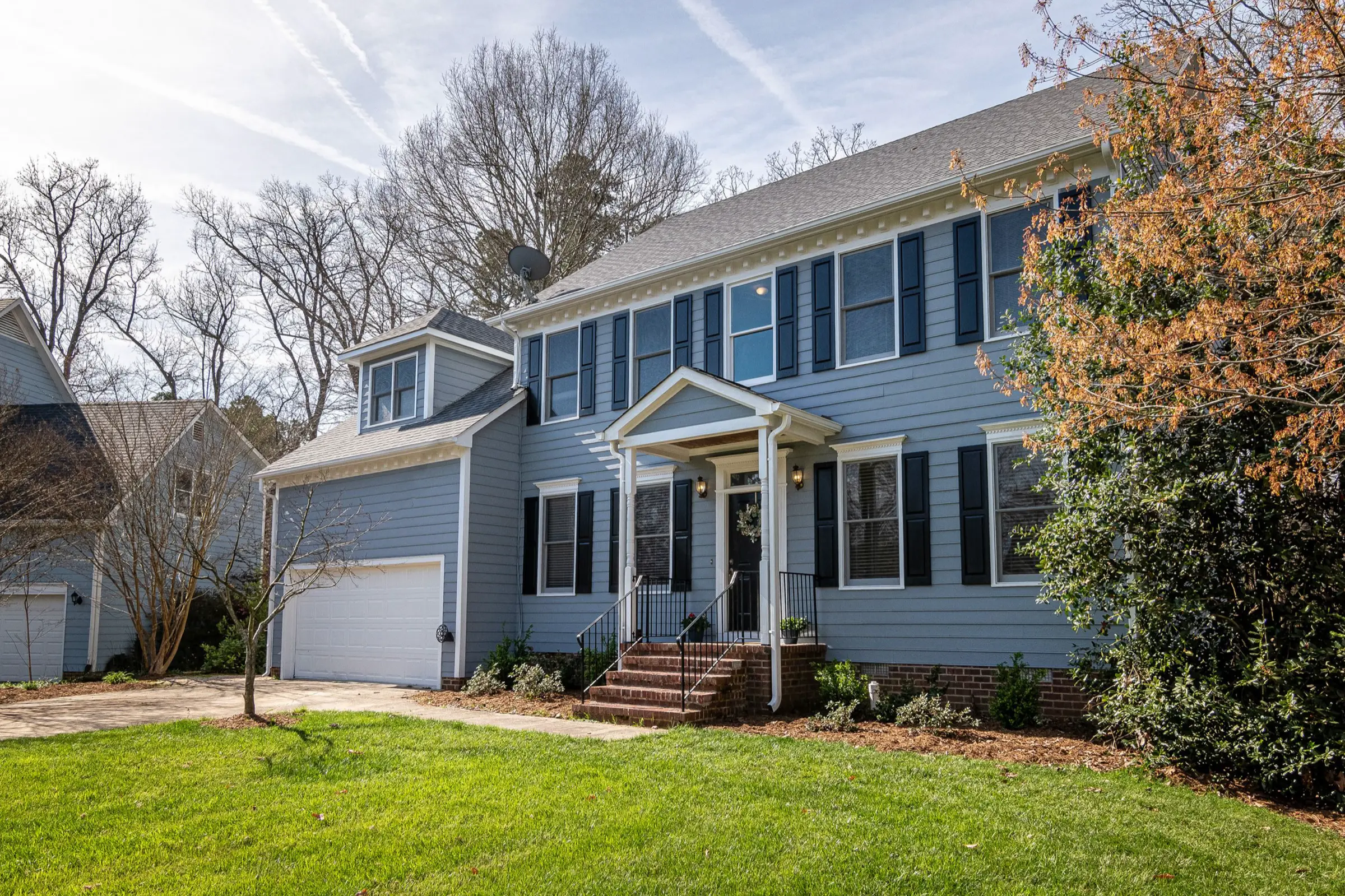 Large blue colonial with black shutters, a gabled porch and a side garage