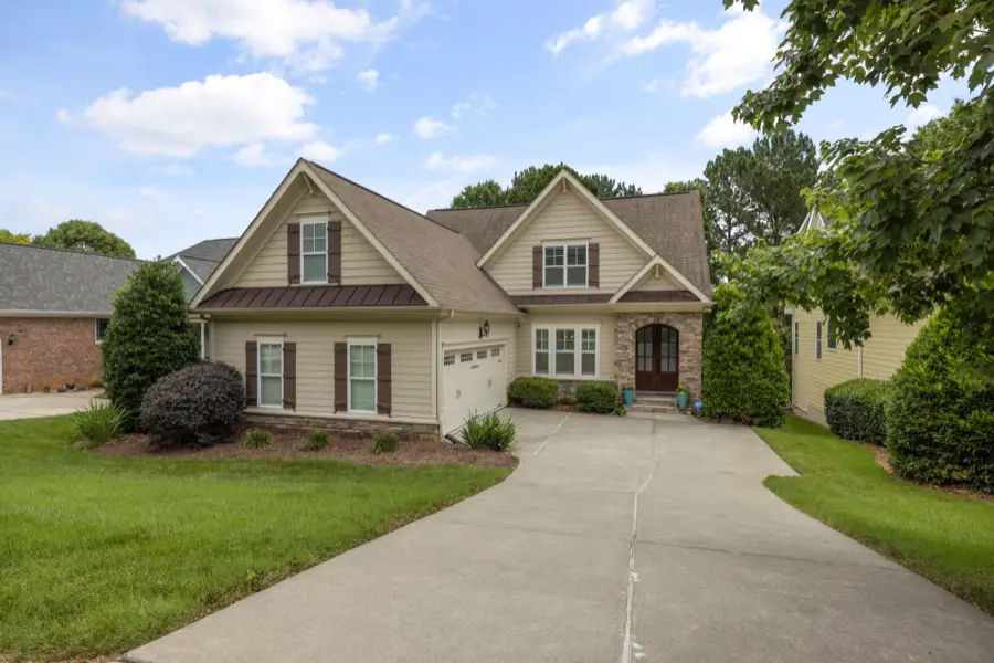 Tan two-story home with twin gables and a long driveway