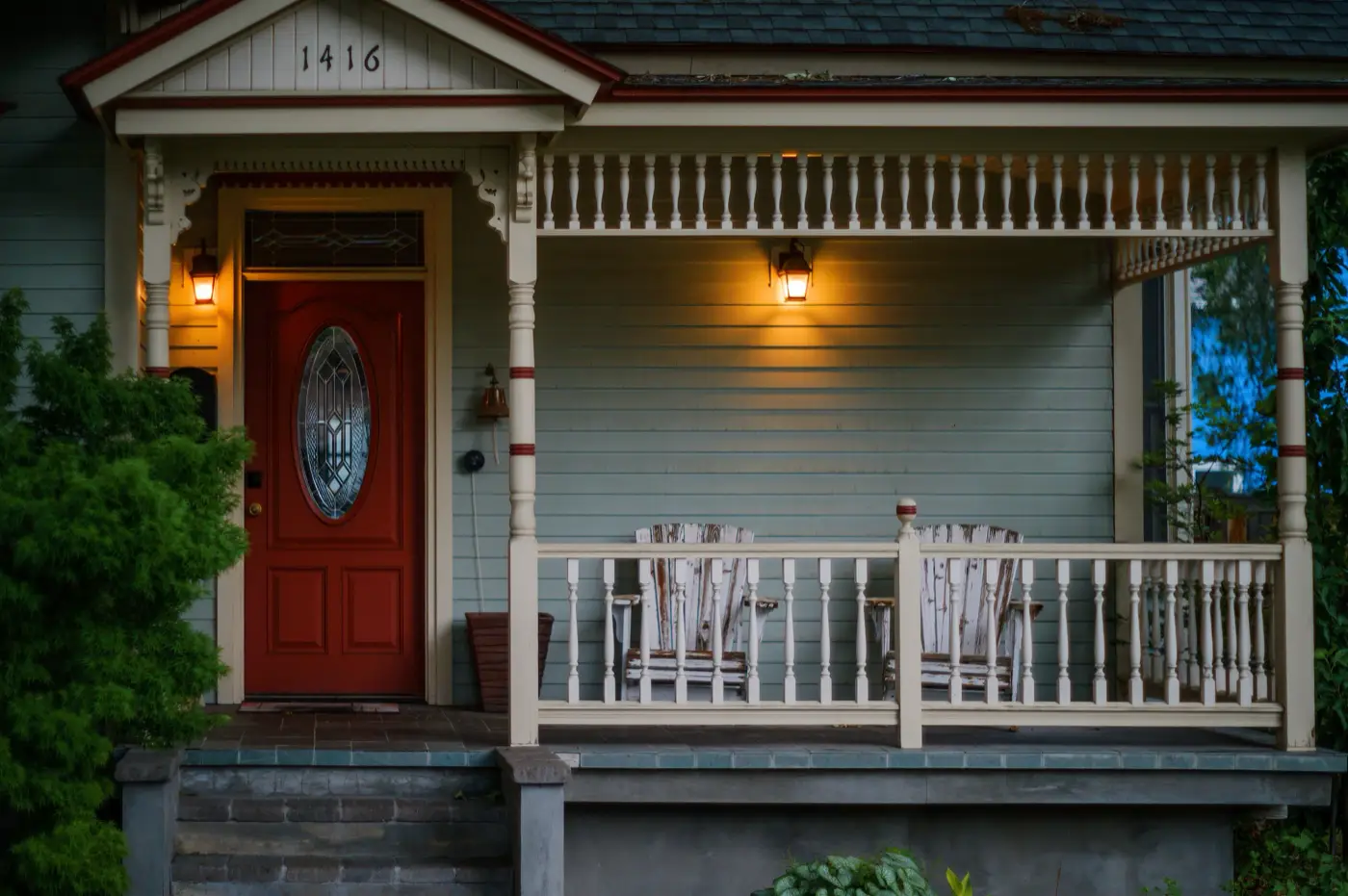 Covered front porch with a red front door and warm porch lights