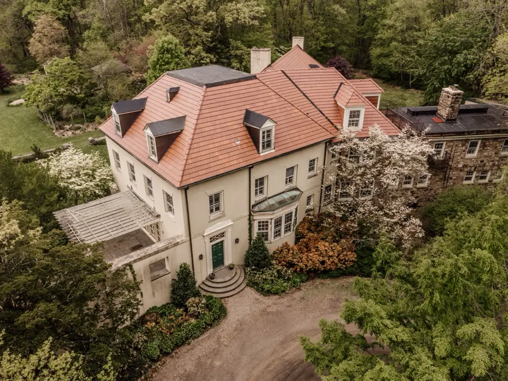 Stucco manor with a terracotta roof and fieldstone wing among flowering dogwoods