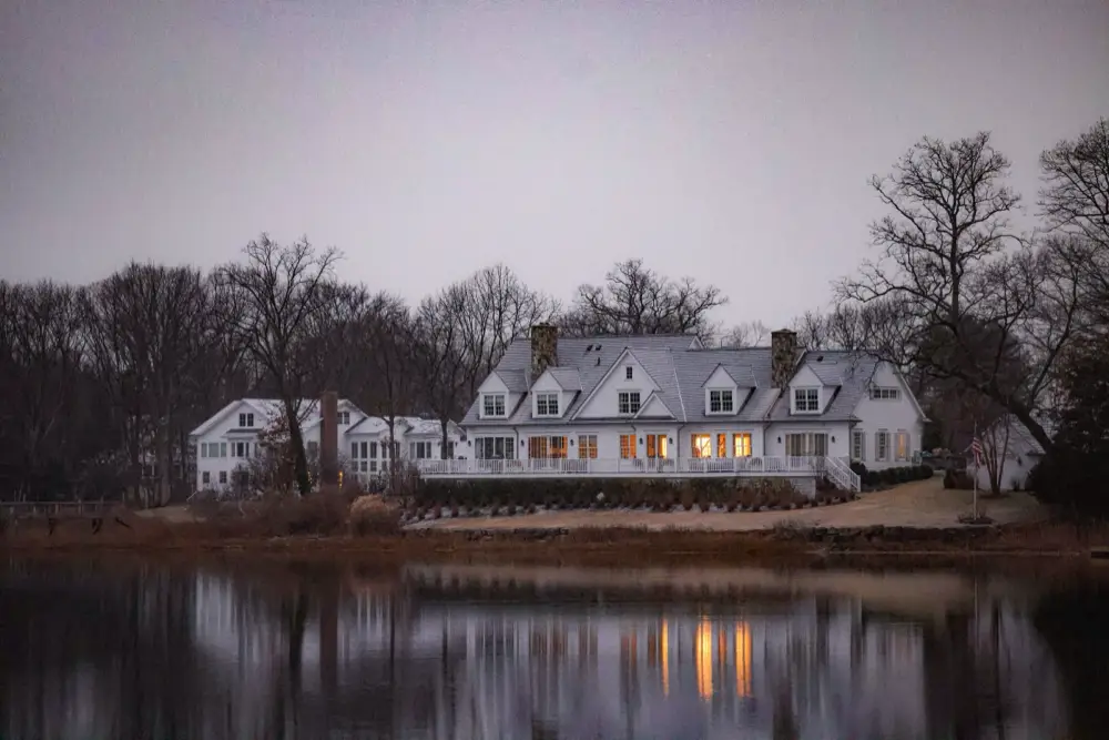 Shingle-style waterfront home lit at dusk